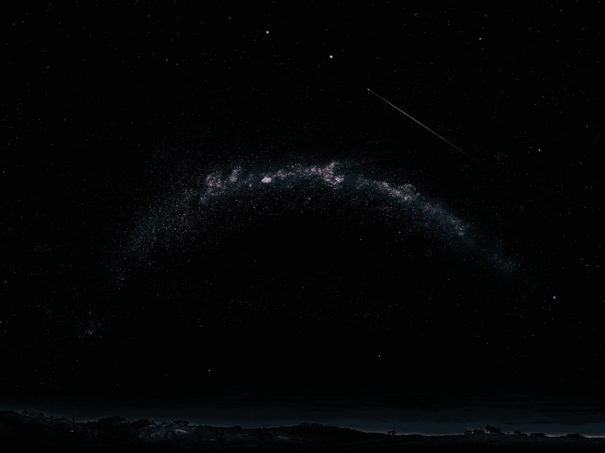 Milky Way arching over a dark countryside with a satellite streak crossing the sky